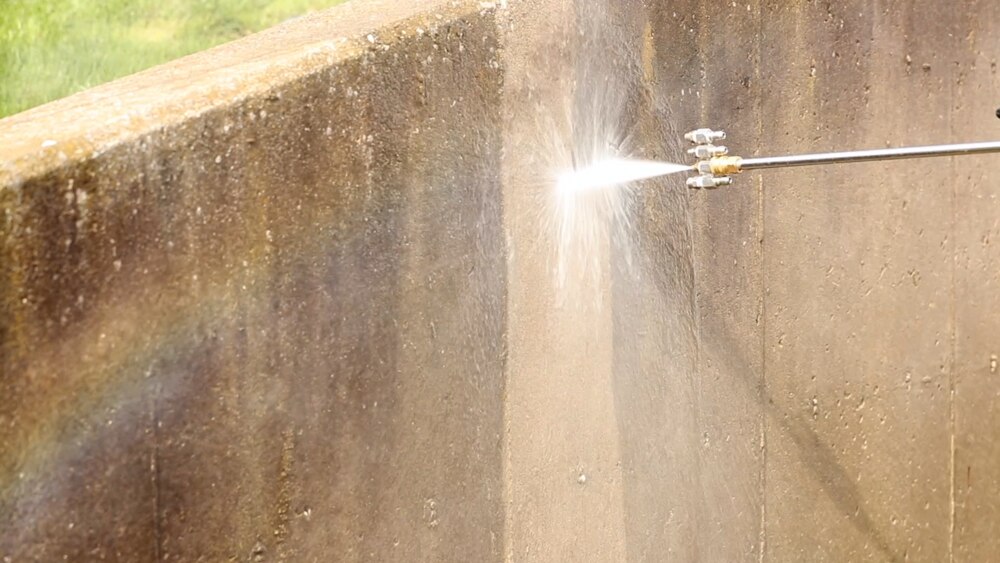High-pressure washing being used to remove dirt and grime from a concrete wall.